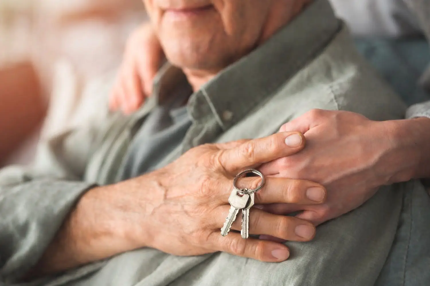 A caregiver holds the hands of an elderly person holding house keys